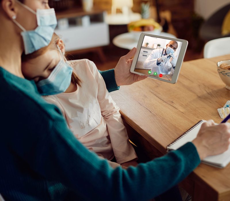 Close-up of mother using digital tablet while talking with pediatrician about her ill daughter during coronavirus pandemic.
