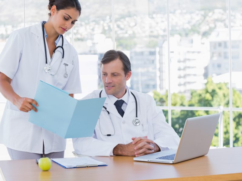 Doctor showing a folder to a colleague sat at his desk