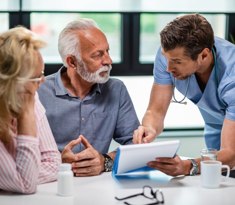 Serious doctor discussing with senior couple about their medical documents during appointment at clinic.